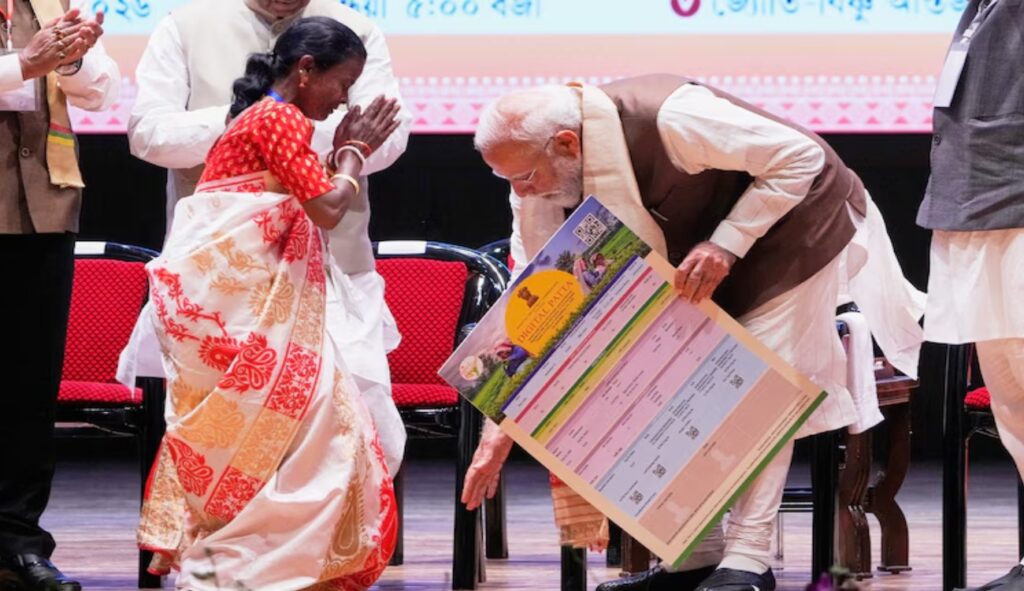 Prime Minister Narendra Modi reaches down to touch the feet of a tea garden worker before he distributes a land title in Guwahati
